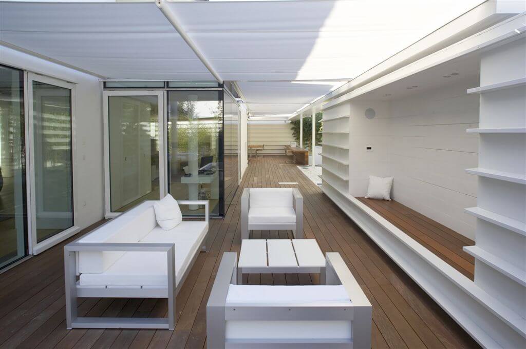 Opposite view of deck area, highlighting the white and metal couch and chairs, shelve-style seating and large glass doors. Opposite view of deck area, highlighting the white and metal couch and chairs, shelve-style seating and large glass doors.