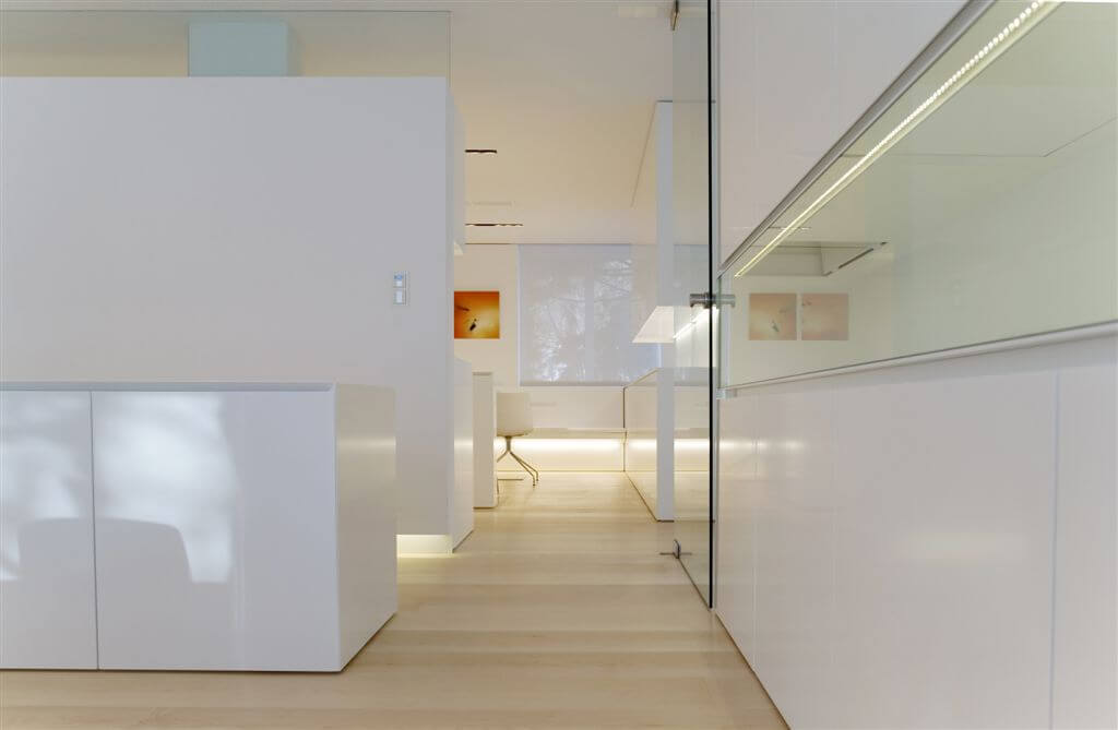 Hallway featuring large expanses of glass set against smooth white surfaces, with corner office area in background. Hallway featuring large expanses of glass set against smooth white surfaces, with corner office area in background.