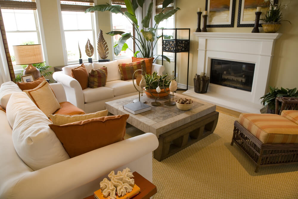 Bright and colorful living room design with off-white sofas decorated with orange and brown pillows. One wall of large windows flood the space with natural light. Bright and colorful living room design with off-white sofas decorated with orange and brown pillows. One wall of large windows flood the space with natural light.
