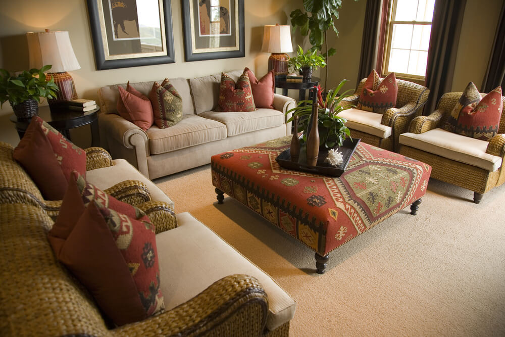 Plush living room in brown and red design. There is one brown sofa and four armchairs all surrounding a patterned ottoman serving as a large coffee table. Brown and red patterned pillows throughout. Plush living room in brown and red design. There is one brown sofa and four armchairs all surrounding a patterned ottoman serving as a large coffee table. Brown and red patterned pillows throughout.