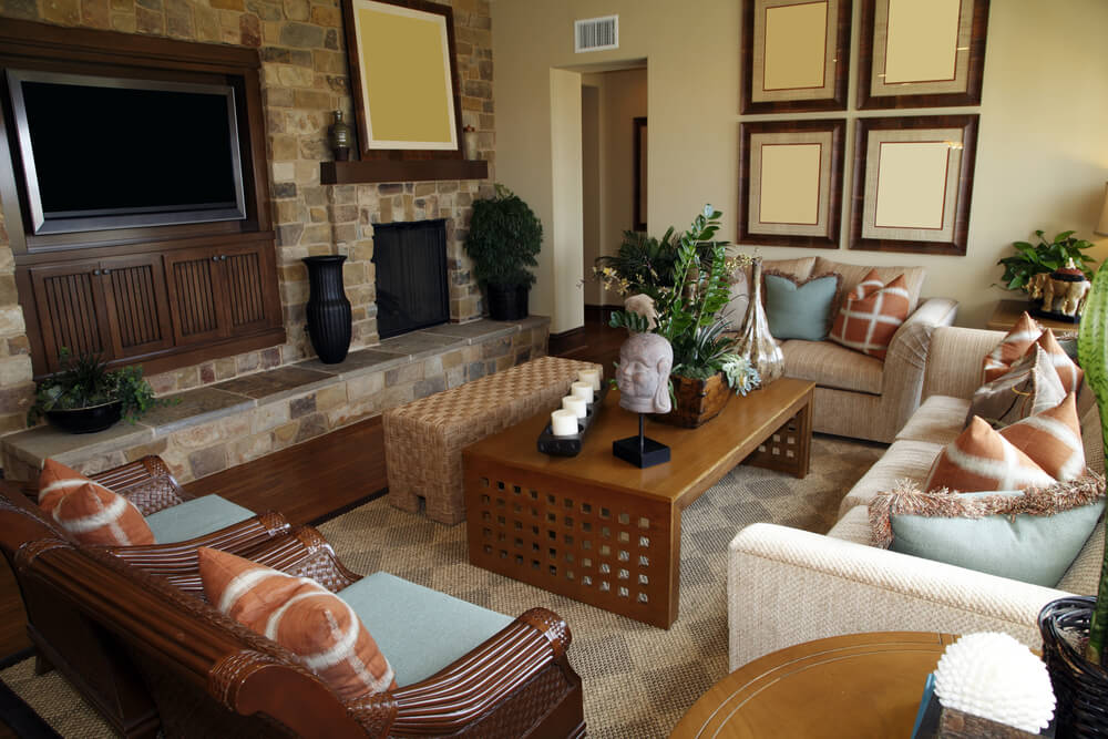 Living room that doubles as family room with one sofa, one loveseat and two ornate wooden chairs all facing flat screen television mounted in wood shelving surrounded by a brick wall. Living room that doubles as family room with one sofa, one loveseat and two ornate wooden chairs all facing flat screen television mounted in wood shelving surrounded by a brick wall.