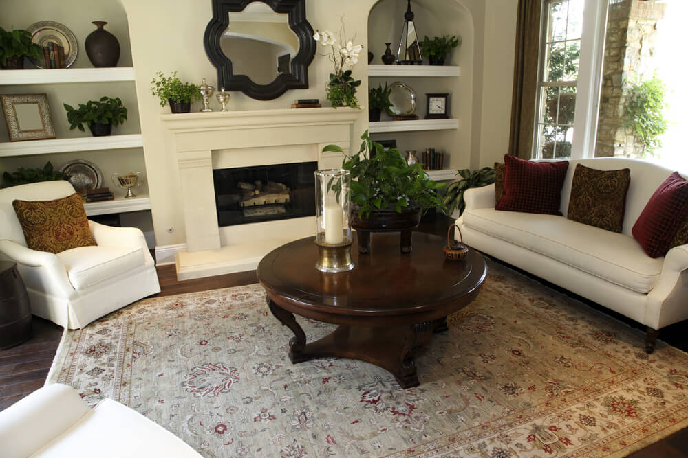 Built-in recessed shelving add depth to this white and dark brown living room design. The built-in shelving frames the white fireplace. Furniture includes two white armchairs, one white sofa and a dark brown round coffee table. Built-in recessed shelving add depth to this white and dark brown living room design. The built-in shelving frames the white fireplace. Furniture includes two white armchairs, one white sofa and a dark brown round coffee table.