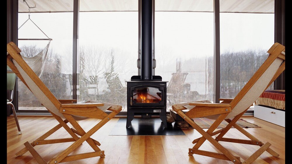 Head on view of black heating stove, seated centrally against the back patio doors over hardwood flooring. Head on view of black heating stove, seated centrally against the back patio doors over hardwood flooring.