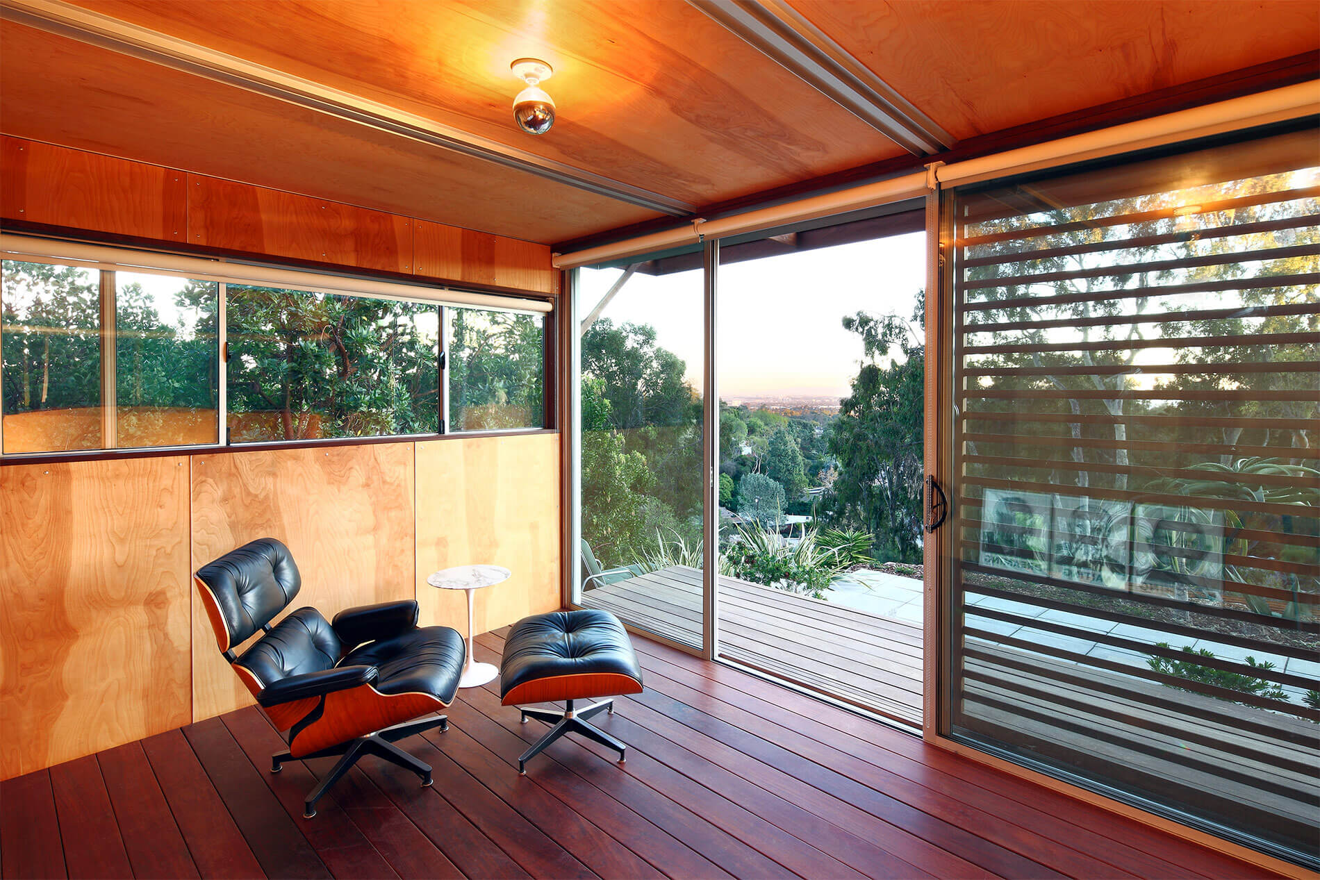 Interior decked out in rich red wood flooring with lighter natural wood walls and ceiling, full glass view of outdoors with shade slats. Interior decked out in rich red wood flooring with lighter natural wood walls and ceiling, full glass view of outdoors with shade slats.