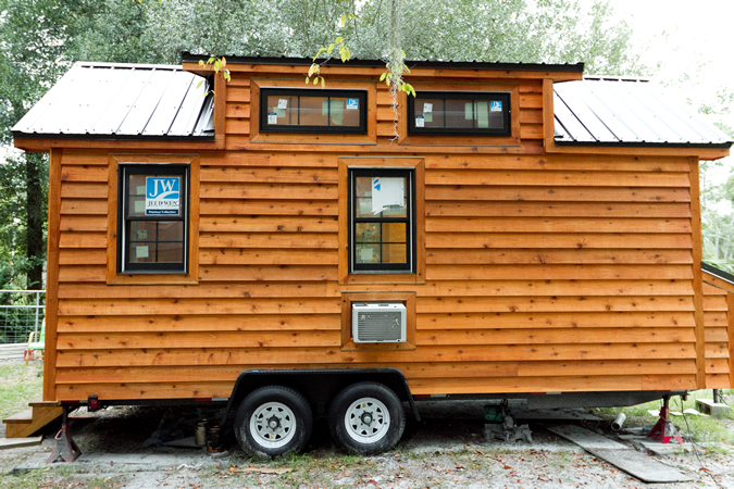 Side view of home, showcasing lower and upper windows, built-in air conditioning unit, and wheels for transport. Side view of home, showcasing lower and upper windows, built-in air conditioning unit, and wheels for transport.