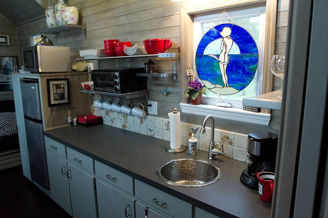 Full featured kitchen holds lengthy black countertop with sink under stained glass window cover, with appliances on left. Full featured kitchen holds lengthy black countertop with sink under stained glass window cover, with appliances on left.