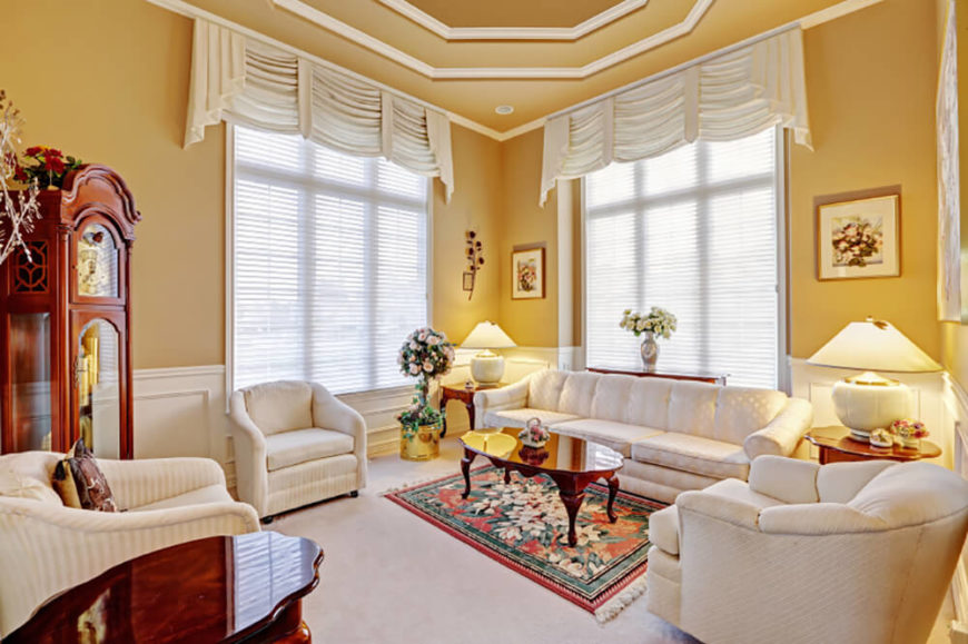 In a traditional, elegant living room, a warm butter yellow on the walls contrasts with the white wainscoting, crown moulding, and furniture. White can seem uninviting sometimes, but a warm color on the walls is a great way to keep the space light and bright. It also draws out the warm undertones of the wooden furniture. In a traditional, elegant living room, a warm butter yellow on the walls contrasts with the white wainscoting, crown moulding, and furniture. White can seem uninviting sometimes, but a warm color on the walls is a great way to keep the space light and bright. It also draws out the warm undertones of the wooden furniture.