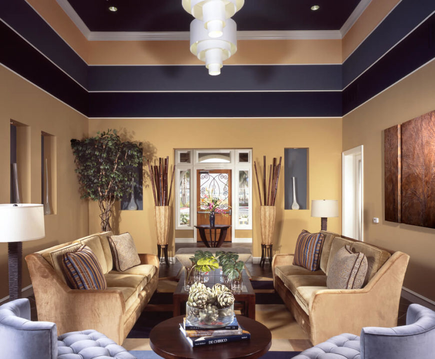 A warm beige on the bottom section of the walls is accented by darker stripes of purple that draw color from the pale lavender chairs on one side of the room. In rooms with tall ceilings, adding treatments to the upper portion of the wall can make a room feel more cozy. A warm beige on the bottom section of the walls is accented by darker stripes of purple that draw color from the pale lavender chairs on one side of the room. In rooms with tall ceilings, adding treatments to the upper portion of the wall can make a room feel more cozy.