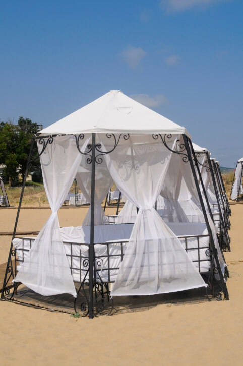 An aluminum gazebo with a canopy top and cushions formed to make a cozy bed-like structure. This gazebo is a luxurious way to relax on the beach and beat the summer heat. An aluminum gazebo with a canopy top and cushions formed to make a cozy bed-like structure. This gazebo is a luxurious way to relax on the beach and beat the summer heat.