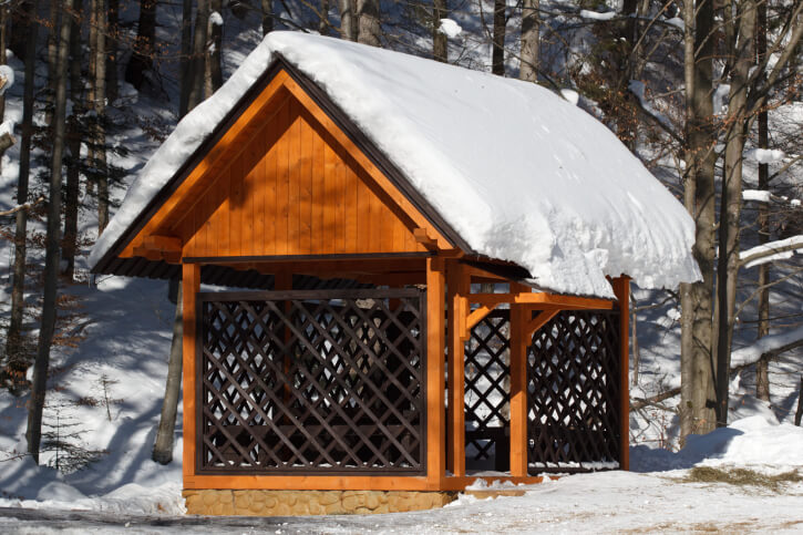 The latticed sides of this gazebo form a kind of screen. The tall gable roof is piled with snow in this stark winter landscape. The latticed sides of this gazebo form a kind of screen. The tall gable roof is piled with snow in this stark winter landscape.