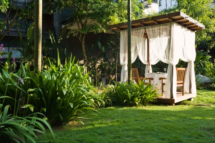 A pergola-styled square gazebo. While it has the grid-structure roof, it's been closed off, making it a gazebo. Sheer curtains add an exotic flair to the structure. A pergola-styled square gazebo. While it has the grid-structure roof, it's been closed off, making it a gazebo. Sheer curtains add an exotic flair to the structure.
