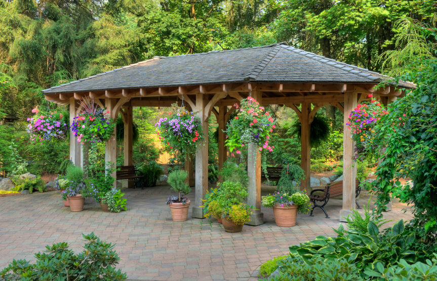 A garden pavilion style gazebo on a brick patio. While the surrounding area is lush, the gazebo stands apart. Hanging baskets and container gardens help integrate the two sections of the yard. A garden pavilion style gazebo on a brick patio. While the surrounding area is lush, the gazebo stands apart. Hanging baskets and container gardens help integrate the two sections of the yard.