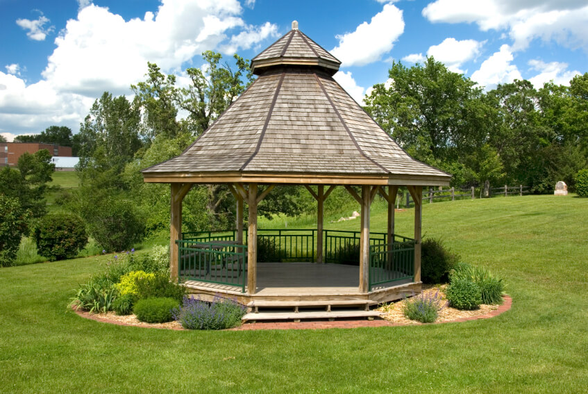 A large wooden gazebo with a two tiered roof, surrounded by shrubs and bushes. The simple landscaping gives this gazebo a pastoral feel. A large wooden gazebo with a two tiered roof, surrounded by shrubs and bushes. The simple landscaping gives this gazebo a pastoral feel.