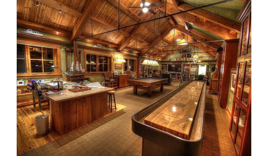A large living area featuring a billiards pool, a living space and an office area all under the wooden vaulted ceiling with exposed beams.