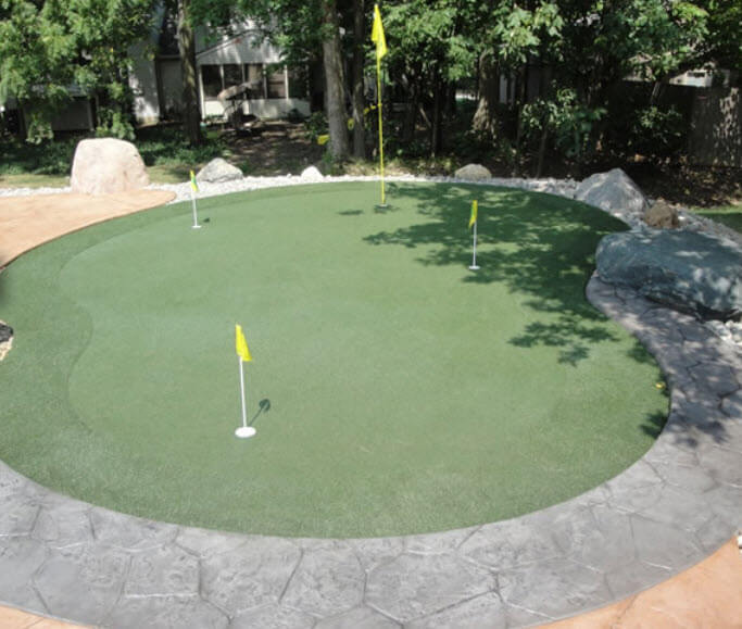 This kidney shaped custom green stands apart from forested space with large stone tile border in grey and sand colors. This kidney shaped custom green stands apart from forested space with large stone tile border in grey and sand colors.