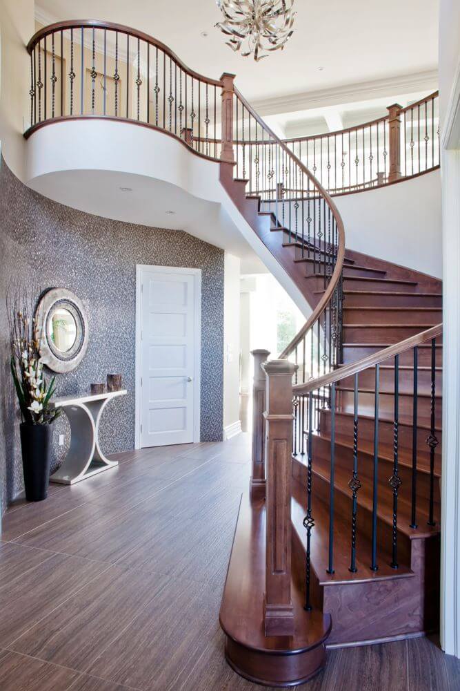 This contemporary foyer has floors with a distinctive wood grain, polished cherry wood stair treads, and a bold patterned wall treatment. A large circular landing overlooks the foyer from the second floor. This contemporary foyer has floors with a distinctive wood grain, polished cherry wood stair treads, and a bold patterned wall treatment. A large circular landing overlooks the foyer from the second floor.