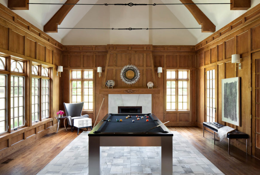 The main spot for guests in this home is the den, which is host to a large billiards table and a series of beautiful, large windows. The center of the floor is a large area rug in geometrics, surrounded by hardwood. On the far wall between two windows is a massive wooden fireplace with a white tile mantle.
