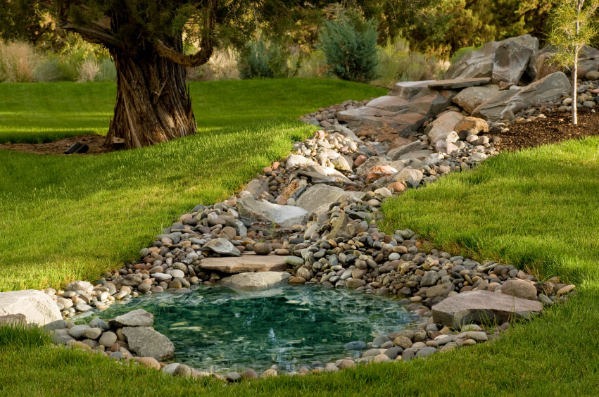 A small, shallow blue pool of water at the bottom of a cascade of stones. Water trickles down through the stones, creating the crystal clear pool at the bottom. A small, shallow blue pool of water at the bottom of a cascade of stones. Water trickles down through the stones, creating the crystal clear pool at the bottom.