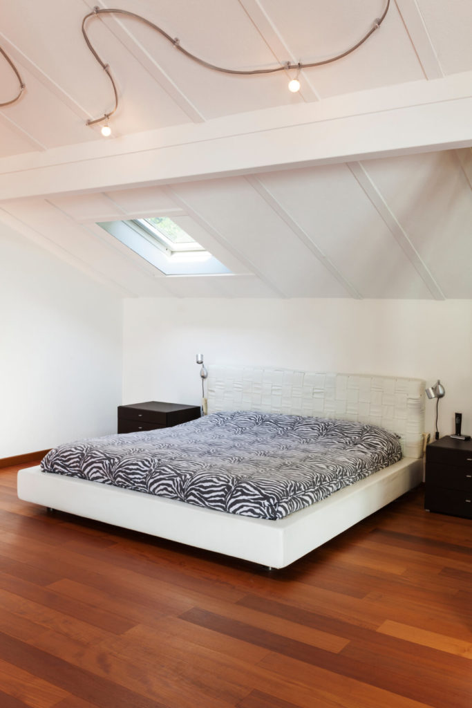 A sleek white platform bed with a textured headboard is combined with a wild zebra pattern, black nightstands, and rich red-toned wood floors. A sleek white platform bed with a textured headboard is combined with a wild zebra pattern, black nightstands, and rich red-toned wood floors.