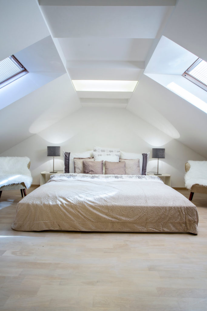 A trio of skylights pour light in from different angles onto the spacious bed. A light color scheme includes natural light hardwood floors. The space is anchored in the complementary color palette of neutrals and natural wood. A trio of skylights pour light in from different angles onto the spacious bed. A light color scheme includes natural light hardwood floors. The space is anchored in the complementary color palette of neutrals and natural wood.