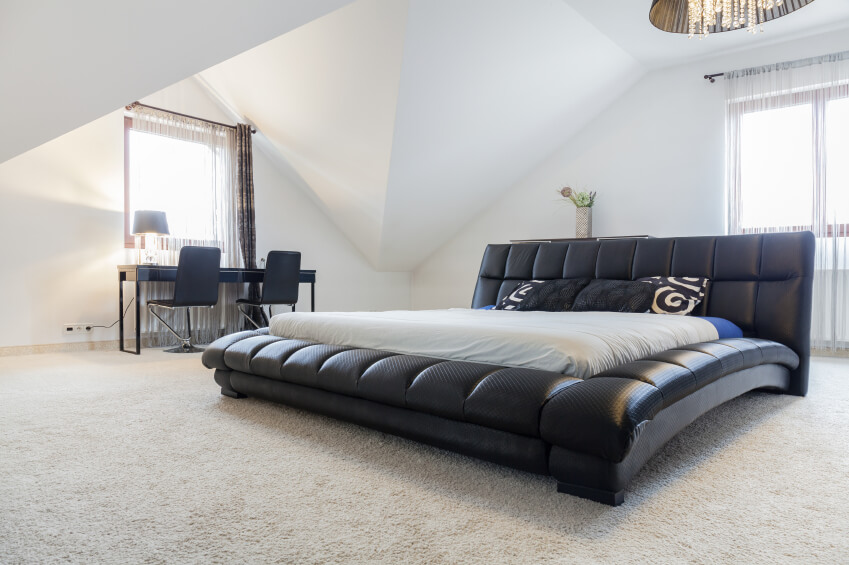 A fantastic faux leather platform bed with curving sides is the focal point of this mostly white bedroom. Sheer curtains cover the large windows. A fantastic faux leather platform bed with curving sides is the focal point of this mostly white bedroom. Sheer curtains cover the large windows.