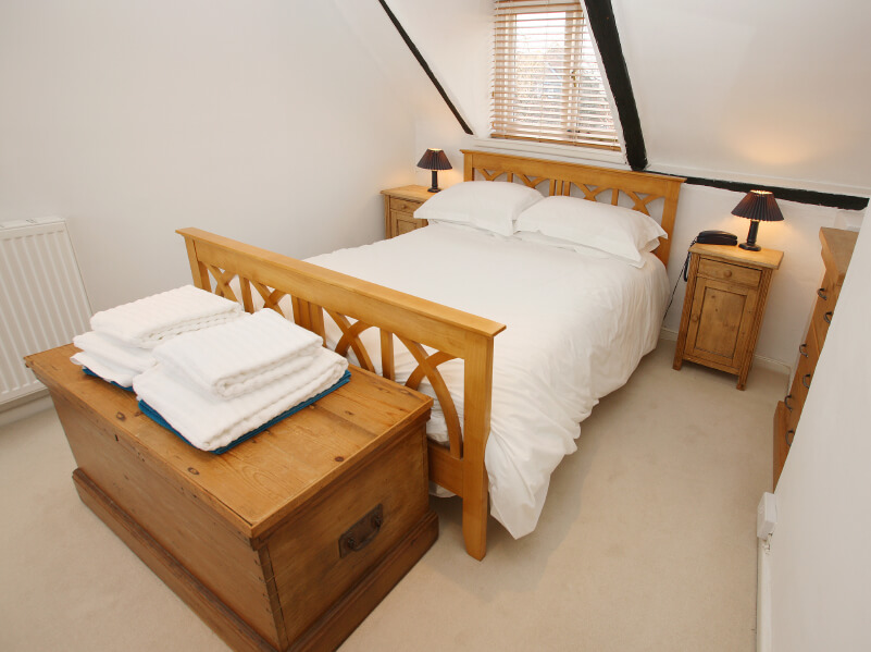 A white bedroom with beautiful natural wood furniture including the dresser, nightstands, bed frame, and a large chest for additional storage in lieu of a closet. A white bedroom with beautiful natural wood furniture including the dresser, nightstands, bed frame, and a large chest for additional storage in lieu of a closet.