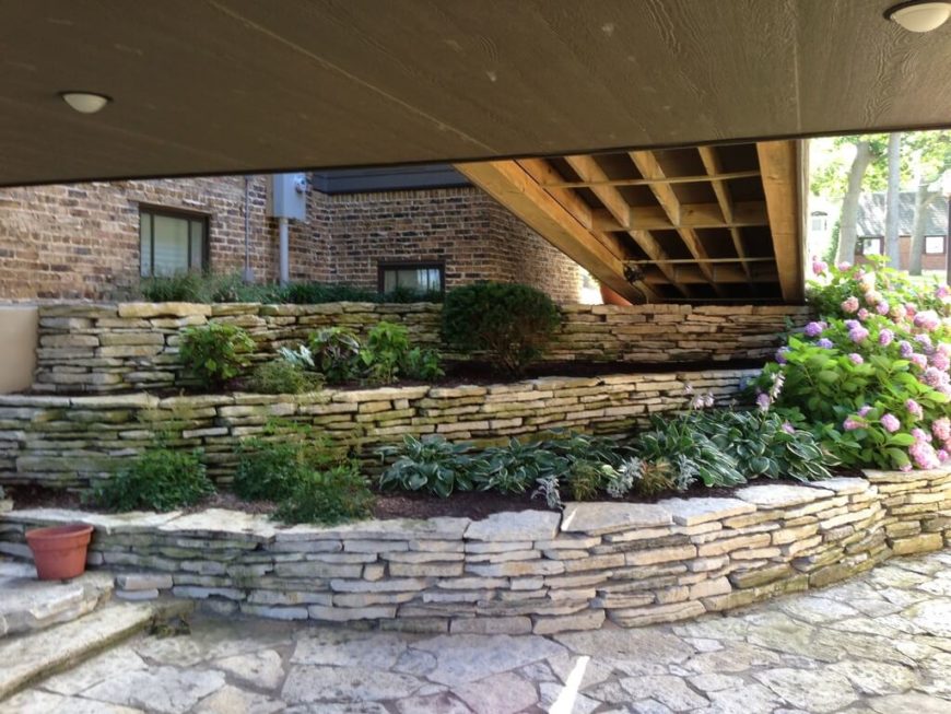 A series of layered stone terraces between the highest and lowest levels of a split-level home. A ramp is overhead. A series of layered stone terraces between the highest and lowest levels of a split-level home. A ramp is overhead.