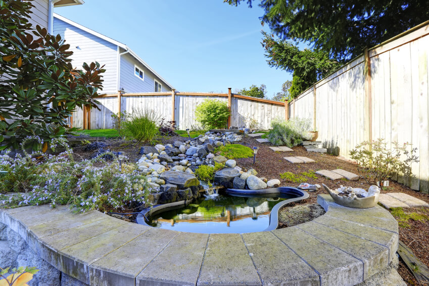 A small garden pool with a stream emptying into the pond. A short wall of stone blocks overlooks the pond. A small garden pool with a stream emptying into the pond. A short wall of stone blocks overlooks the pond.
