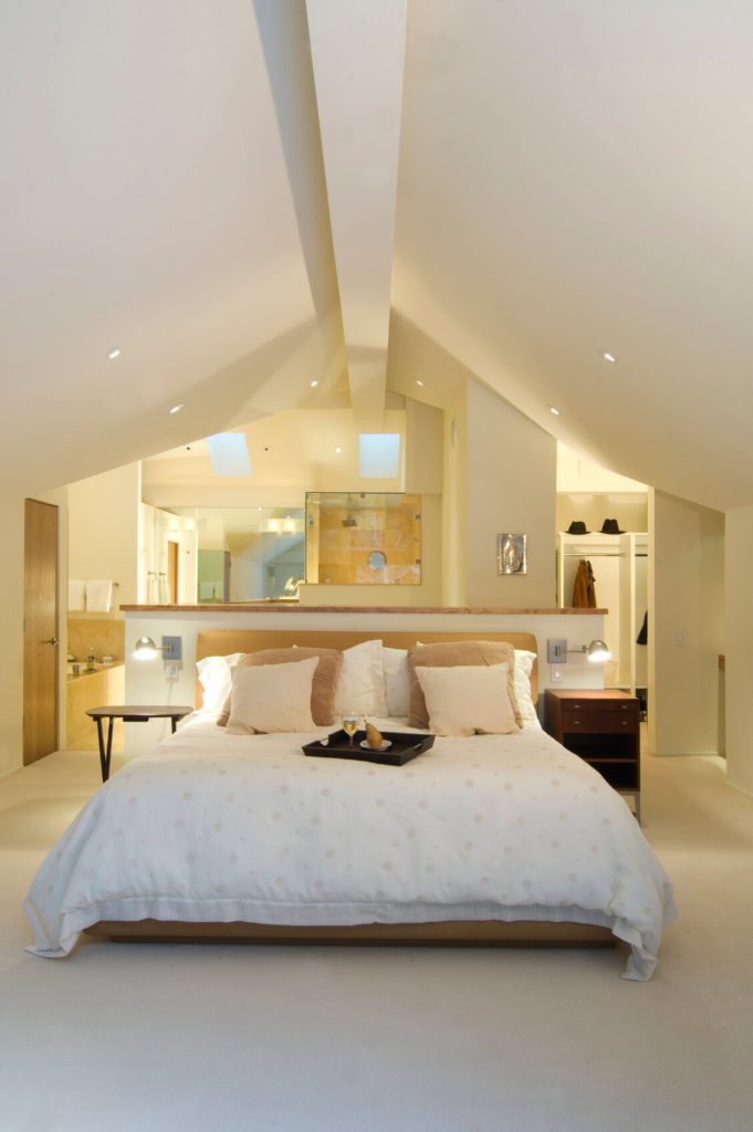 An open concept attic space houses a bedroom, closet, and bathroom. The bed is situated against a half-wall, creating a separate-yet-together feeling to this attic apartment. An open concept attic space houses a bedroom, closet, and bathroom. The bed is situated against a half-wall, creating a separate-yet-together feeling to this attic apartment.