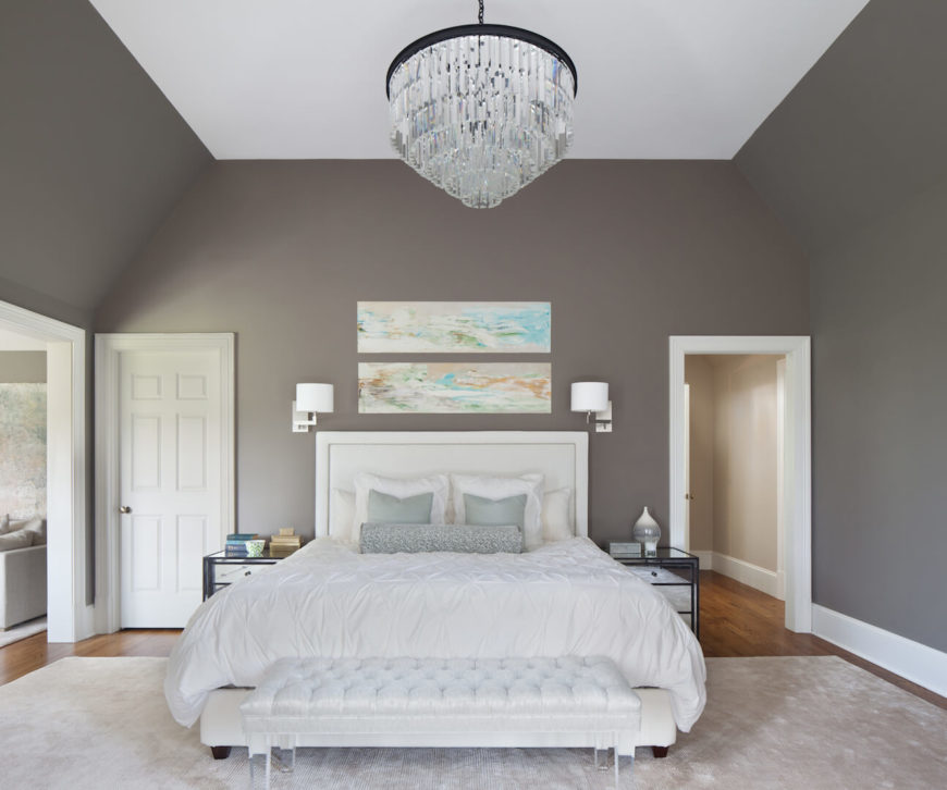 The primary suite has a delicate, light color palette with a gray-green rich wall color and mint accents. Bolder, yet still elegant colors are brought into the room via the two paintings above the head board. Through the archway on the left is the adjoining sitting room.