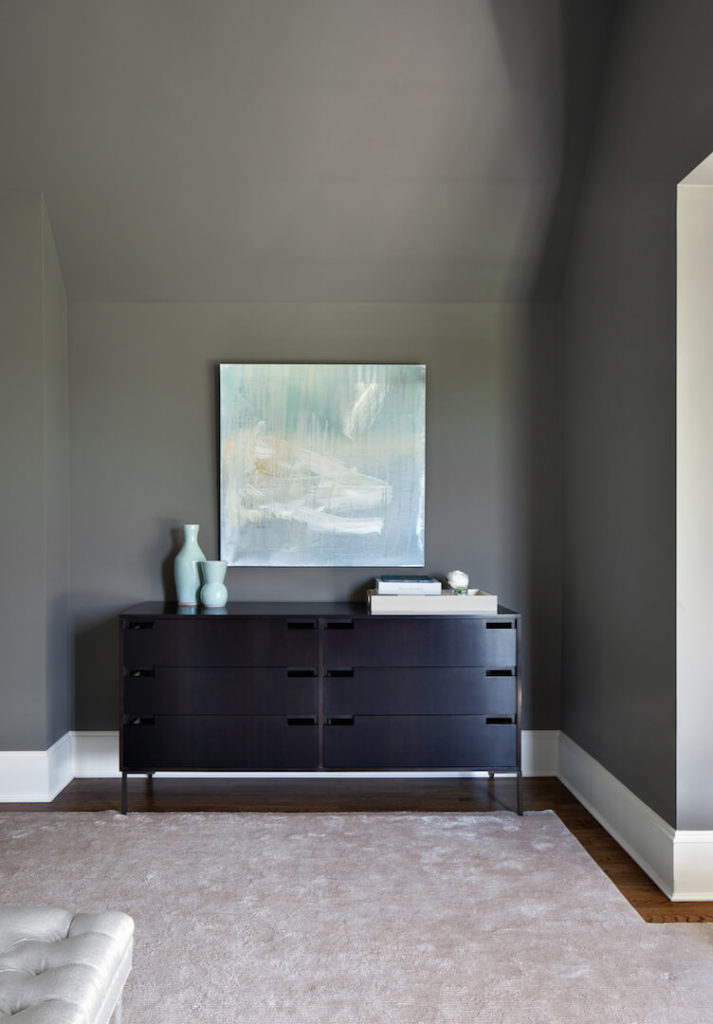 A small nook on the right side of the room is host to a modern-style dresser in a darker wood. The mint from the bed pillows is complemented by the mint pottery on the dresser and the soft water color painting above the dresser.