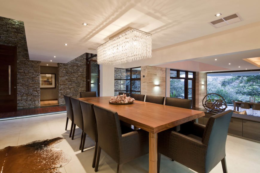 Elegant dining room designed with a gorgeous chandelier that hung over a wooden dining table paired with black cushioned chairs.