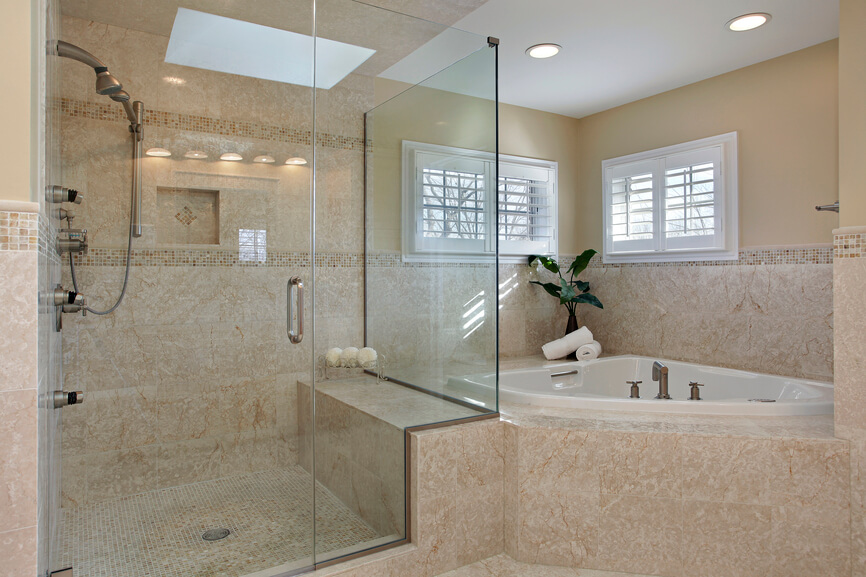 The skylight in this bathroom can be seen in reflection on the clear glass doors of the enclosed shower space. The deep creamy beige of the tiled walls is textured with the natural veins of the stone. More intricate tile-work is noted on the floor of the shower space, and is mimicked around the perimeter. The skylight in this bathroom can be seen in reflection on the clear glass doors of the enclosed shower space. The deep creamy beige of the tiled walls is textured with the natural veins of the stone. More intricate tile-work is noted on the floor of the shower space, and is mimicked around the perimeter.