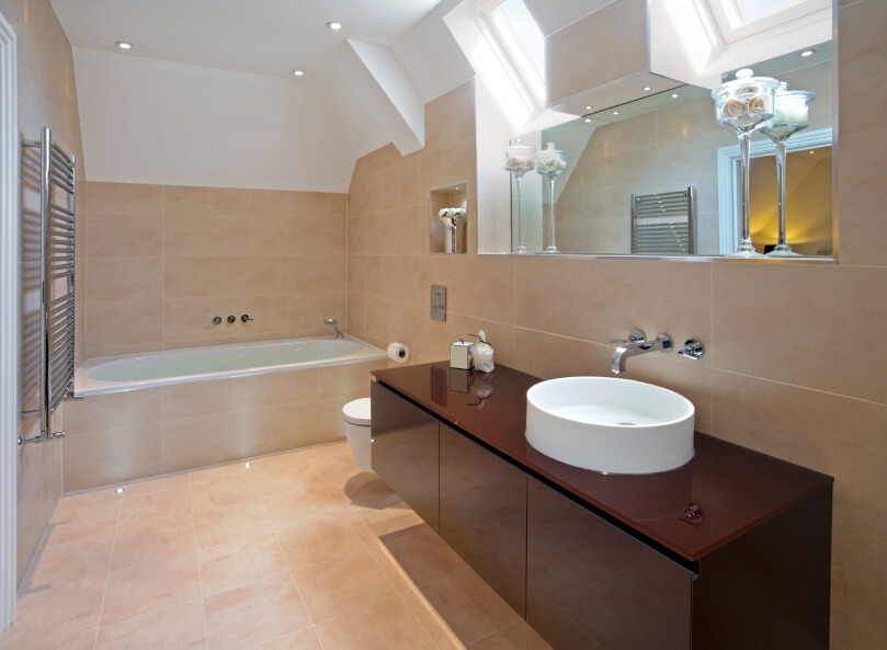 Skylights find their home above a large mirror overlooking a striking modern vanity with unusual basin. The rich, dark wood of the vanity offers interest in contrast to the rest of the creamy peach tiled space. Skylights find their home above a large mirror overlooking a striking modern vanity with unusual basin. The rich, dark wood of the vanity offers interest in contrast to the rest of the creamy peach tiled space.