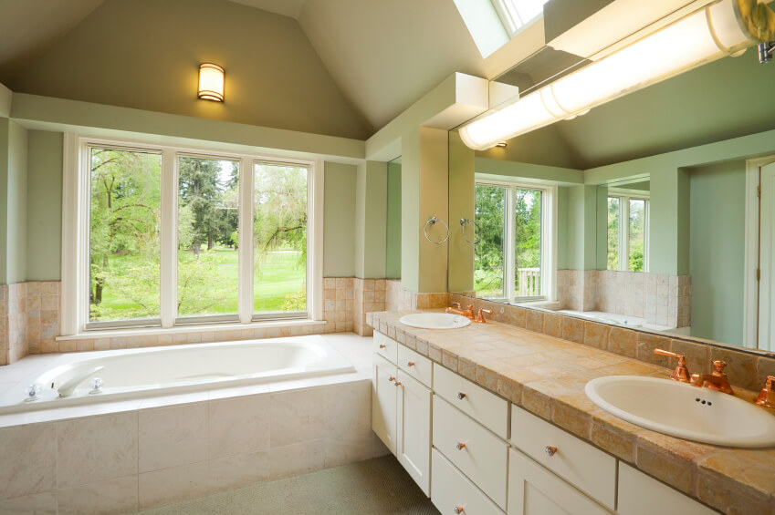 This charming bathroom is rich in ivory, beiges, and mint hues. The stone countertops of the double vanity offer an aesthetically pleasing option with gorgeous texture. Lighting fixtures look down upon the space offering the soft glow of conventional lighting, while a large window and skylight combine to brighten the area. This charming bathroom is rich in ivory, beiges, and mint hues. The stone countertops of the double vanity offer an aesthetically pleasing option with gorgeous texture. Lighting fixtures look down upon the space offering the soft glow of conventional lighting, while a large window and skylight combine to brighten the area.