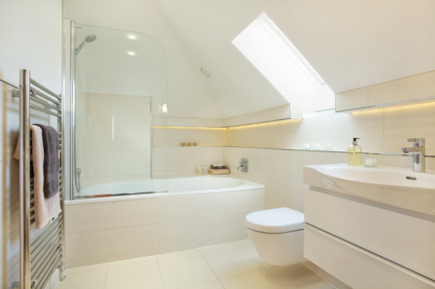This snow-white bathroom space is bright and clean. A tankless modern toilet sits beside the wide sink basin, while a simple bathtub with a glass splashguard is not far away. Soft tracks of lighting run along the rooms perimeter, while a skylight brings additional light to the area. This snow-white bathroom space is bright and clean. A tankless modern toilet sits beside the wide sink basin, while a simple bathtub with a glass splashguard is not far away. Soft tracks of lighting run along the rooms perimeter, while a skylight brings additional light to the area.