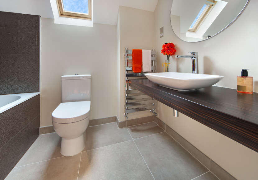 The lovely wood countertop has exquisite graining, while a modern basin sits elegantly on top. A stainless steel towel rack holds decorative hand towels, offering a bright splash of color coordinating with a small floral arrangement. A skylight hovers above the toilet and bathing area. The lovely wood countertop has exquisite graining, while a modern basin sits elegantly on top. A stainless steel towel rack holds decorative hand towels, offering a bright splash of color coordinating with a small floral arrangement. A skylight hovers above the toilet and bathing area.