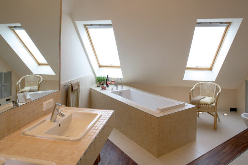 Double skylights filter light upon the finely tiled narrow bathtub. Glasses of wine are already prepared for a long relaxing soak, while the matching double vanity offers ample space. Large white ceramic tiles protect the hardwood floor from water damage, and a simple natural wood chair is on hand for comfortable bath preparations. Double skylights filter light upon the finely tiled narrow bathtub. Glasses of wine are already prepared for a long relaxing soak, while the matching double vanity offers ample space. Large white ceramic tiles protect the hardwood floor from water damage, and a simple natural wood chair is on hand for comfortable bath preparations.