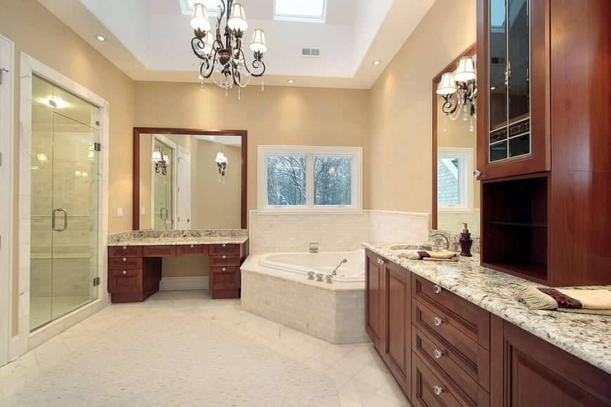 This luxury bathroom features rich wood cabinetry topped with fine marble. The light tile flooring coordinates with tile encasing the bathtub, while the darker walls offer a subtle contrast. Two skylights join an opulent chandelier, while a glass enclosed shower stands to the side. This luxury bathroom features rich wood cabinetry topped with fine marble. The light tile flooring coordinates with tile encasing the bathtub, while the darker walls offer a subtle contrast. Two skylights join an opulent chandelier, while a glass enclosed shower stands to the side.