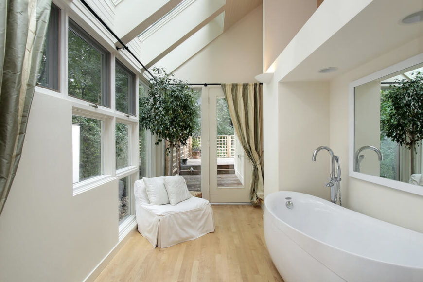 Several skylights and unique window arrangements make this small bathroom space feel open and free. The light hardwood flooring complements the white modern bathtub and contrasts with the sage and olive drapery, while a view of a patio area can be seen through the door. Several skylights and unique window arrangements make this small bathroom space feel open and free. The light hardwood flooring complements the white modern bathtub and contrasts with the sage and olive drapery, while a view of a patio area can be seen through the door.