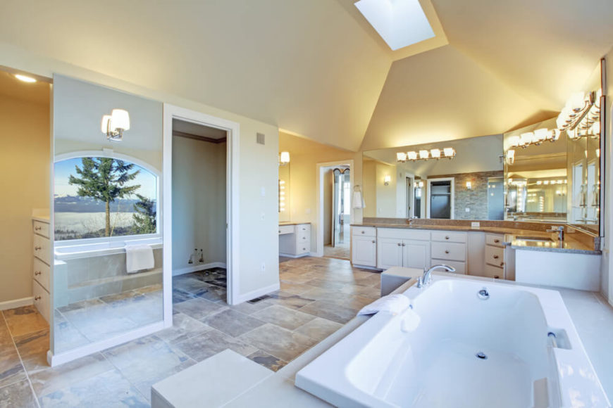 An absolutely breathtaking bathroom offers plenty of radiant light, soaring ceilings, and an arched picture window reflecting into a mirrored wall panel. The numerous mirrors and high ceilings contribute to the open, airy feel of this already sizable bathroom. A skylight shines down additional light, while large stone tiles offer interest and variation. An absolutely breathtaking bathroom offers plenty of radiant light, soaring ceilings, and an arched picture window reflecting into a mirrored wall panel. The numerous mirrors and high ceilings contribute to the open, airy feel of this already sizable bathroom. A skylight shines down additional light, while large stone tiles offer interest and variation.