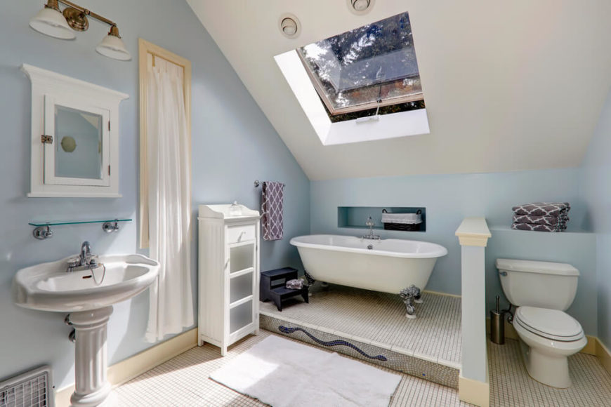 This charming bathroom features an extravagant clawfoot tub, painted white cabinetry, a traditional pedestal sink, and a beautiful mosaic at the base of the bathing area. A skylight allows healthy rays to filter through to brighten the powder blue and white space. This charming bathroom features an extravagant clawfoot tub, painted white cabinetry, a traditional pedestal sink, and a beautiful mosaic at the base of the bathing area. A skylight allows healthy rays to filter through to brighten the powder blue and white space.