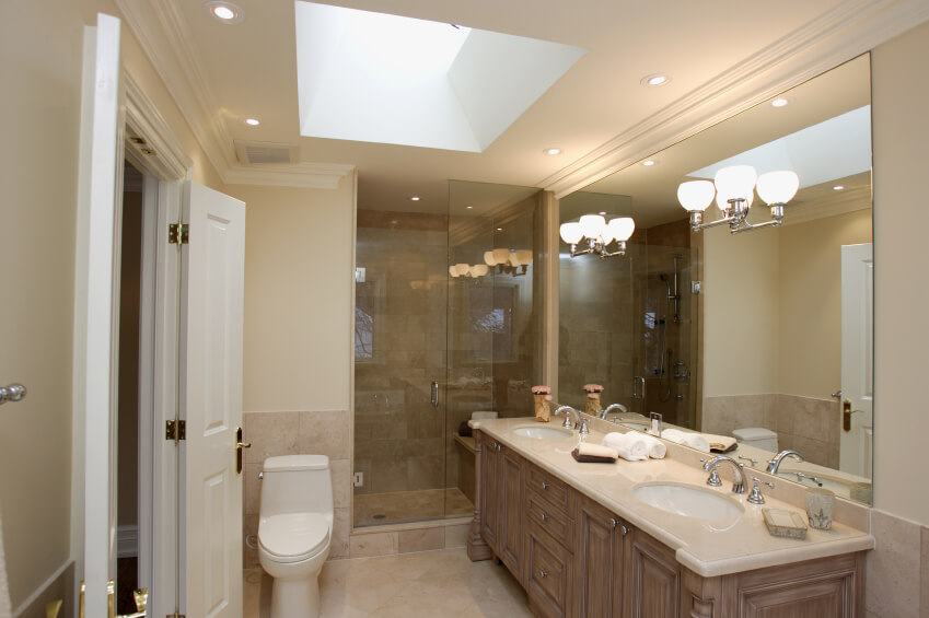 Mirror sconces, recessed lighting, and a skylight work together to highlight this lovely bathroom space. A toilet is positioned precariously close to the door, and a glass enclosed shower beckons use. A creamy porcelain topped double vanity takes up residence, offering plenty of space for daily preparations. Mirror sconces, recessed lighting, and a skylight work together to highlight this lovely bathroom space. A toilet is positioned precariously close to the door, and a glass enclosed shower beckons use. A creamy porcelain topped double vanity takes up residence, offering plenty of space for daily preparations.