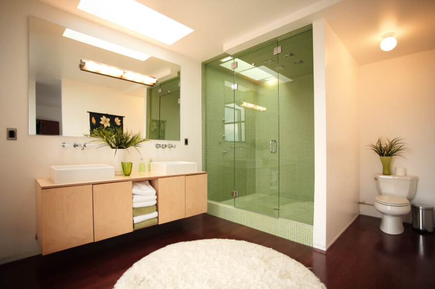 This attractive bathroom features a simple skylight and lighting fixtures to maximize light within the space. The ivory walls contrast beautifully with the dark hardwood, with the plush, round area rug offers further contrast. The deep olive tile work of the glass enclosed shower is a thoughtful design choice and is mimicked in numerous accents throughout the room. This attractive bathroom features a simple skylight and lighting fixtures to maximize light within the space. The ivory walls contrast beautifully with the dark hardwood, with the plush, round area rug offers further contrast. The deep olive tile work of the glass enclosed shower is a thoughtful design choice and is mimicked in numerous accents throughout the room.