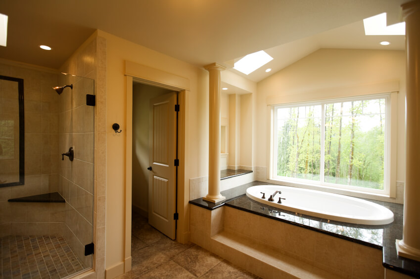 Multiple skylights working in unison with a tub-side picture window call this beautiful bathroom space their home. The bathtub encasement is topped with a dark stone for contrast, while a step leads the way for easy access. Multiple skylights working in unison with a tub-side picture window call this beautiful bathroom space their home. The bathtub encasement is topped with a dark stone for contrast, while a step leads the way for easy access.