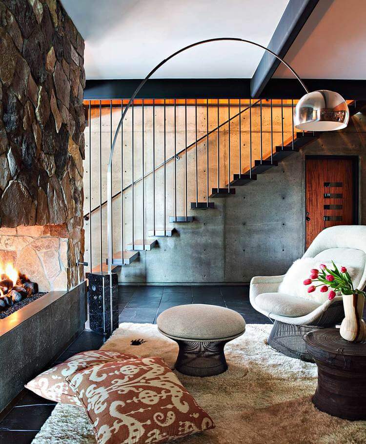 A chrome arched floor lamp illuminates this living room offering a stone fireplace facing comfy seats and coffee tables that sit on a beige shaggy rug.