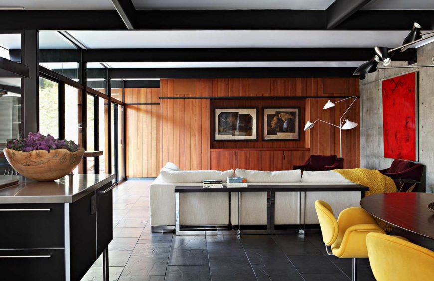 Mid-century modern living room decorated with lovely photo frames and a bursting red canvas that hung above the red velvet armchair accompanied by a white sectional and metal console table.