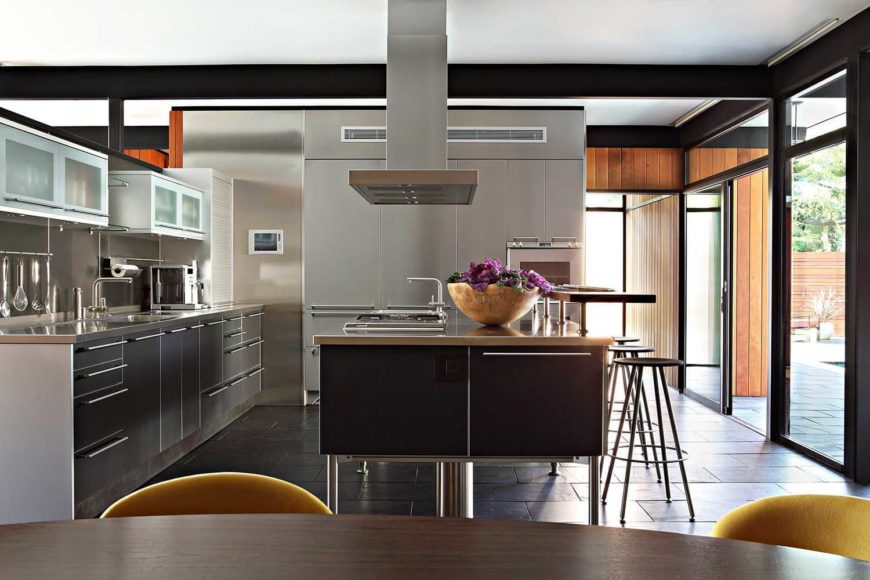 Modern palette L-shaped kitchen with gray drawers, breakfast island, black tiles floors, and glass sliding doors.