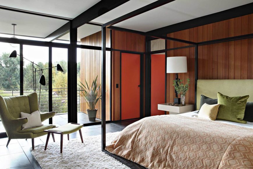 This mid-century modern primary bedroom boasts a large bed and a black shade surrounding the room. It features glass walls overlooking the outdoor views.