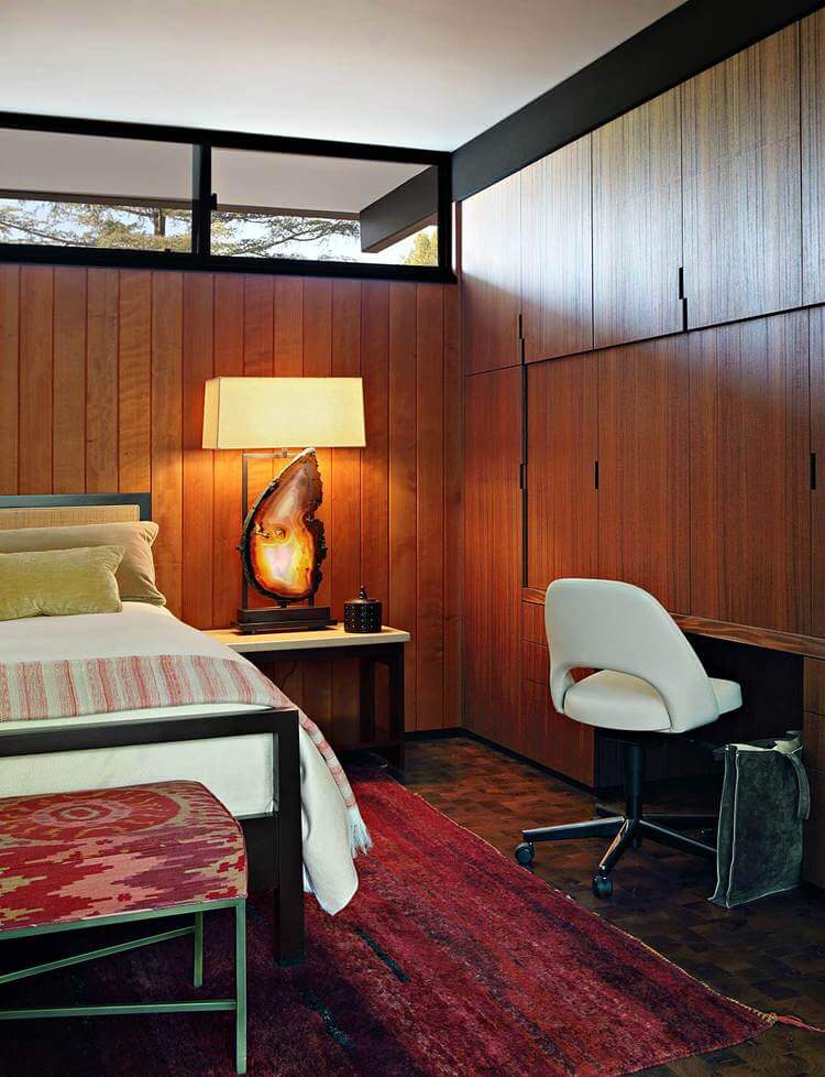 Mid-century modern primary bedroom with tiles flooring topped by a large area rug and is surrounded by rustic walls lighted by warm white lighting.